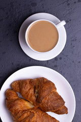a white ceramic cup of black roasted coffee espresso and a french croissant on the wooden surface