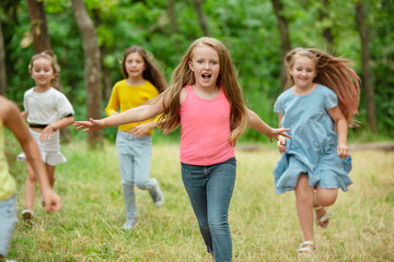 Fototapeta premium Memories. Kids, children running on green forest. Cheerful and happy boys and girs playing, laughting, running through green blooming meadow. Childhood and summertime, sincere emotions concept.