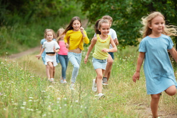 Memories. Kids, children running on green forest. Cheerful and happy boys and girs playing, laughting, running through green blooming meadow. Childhood and summertime, sincere emotions concept.