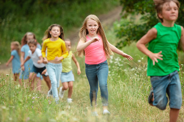 Fototapeta na wymiar Summer. Kids, children running on green forest. Cheerful and happy boys and girs playing, laughting, running through green blooming meadow. Childhood and summertime, sincere emotions concept.