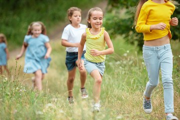 Fototapeta premium Summer. Kids, children running on green forest. Cheerful and happy boys and girs playing, laughting, running through green blooming meadow. Childhood and summertime, sincere emotions concept.