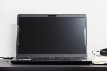 black laptop show blank screen place on desk with white wall isolated