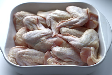 Chicken wings with skin in a white glass plate. Ingredients, fresh, cut meat for cooking. Chicken parts, protein. Diet meat
