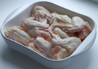 Chicken wings with skin in a white glass plate. Ingredients, fresh, cut meat for cooking. Chicken parts, protein. Diet meat
