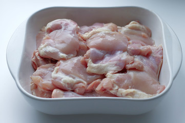 Chicken thigh fillet with skin, in a white glass plate, on a gray background. Ingredients, fresh, cut meat for cooking. Chicken parts, protein. Diet meat, fillet in a plate