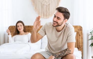 Solving problems in bed. Smiling man holding in hand blue pill, woman looking at husband