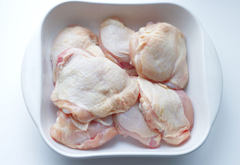 chicken thighs with skin, in a white glass plate, on a gray background. Ingredients, fresh, sliced meat for cooking. Chicken parts, protein. Diet meat, fillet in a plate. Place for text