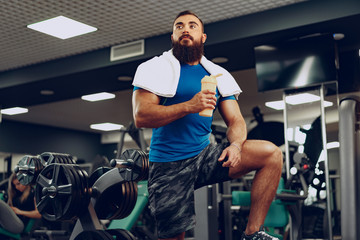Fototapeta na wymiar Bearded young man bodybuilder in blue t-shirt standing in gym