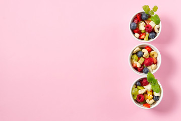 Bowl of healthy fresh fruit salad on pink background, top view copy space.