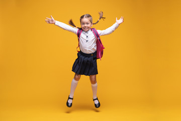 Joyful little school girl jumping over yellow background. Happiness, activity and child concept