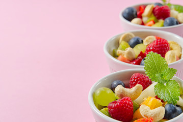 Bowl of healthy fresh fruit salad on pink background, side view copy space.