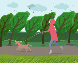 Walk with dog in the park. Woman is running with a doggy in garden strong windy weather. A happy pet walking with the owner against the backdrop of autumn landscape with a green trees bent to ground