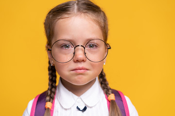 Portrait sad little girl standing on a yellow background.
