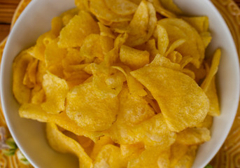 Crispy potato chips in bowl on wooden table, top view. Unhealthy eating concept. Close-up. Selective focus.