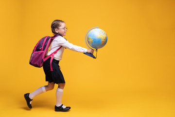 a little girl in school uniform holds a globe in her hands on a yellow background