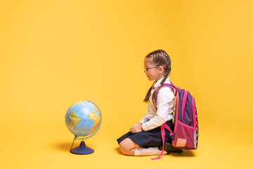 a little girl in school uniform holds a globe in her hands on a yellow background