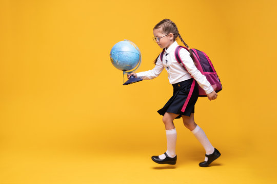 a little girl in school uniform holds a globe in her hands on a yellow background - Powered by Adobe