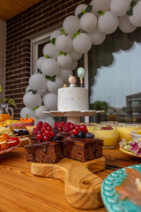 First anniversary party. Chocolate cake with berries on a wooden plate. Delicious desserts on rustic wooden table with the anniversary cake in the background. Diversity of pastry decorated with fruit.