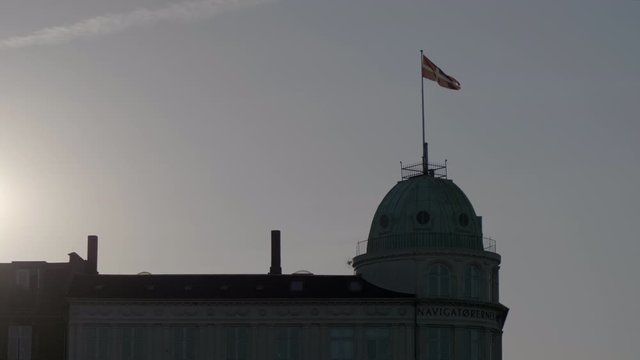 The danish flag Dannebrog waving in the wind at the top of a building in Copenhagen at sunset. Danish flag stock footage
