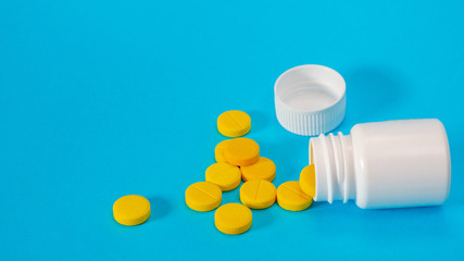 Yellow pills and plastic white bottle. Blue background with copy space for text. Healthy and medicine. Pain management. Drug abuse in teenage concept