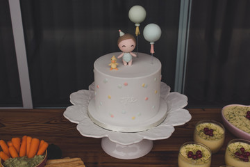 First Anniversary party. A beautiful first birthday stylish white cake decorated with balloons, a little boy figure and his cute duckling. The concept of festive desserts.