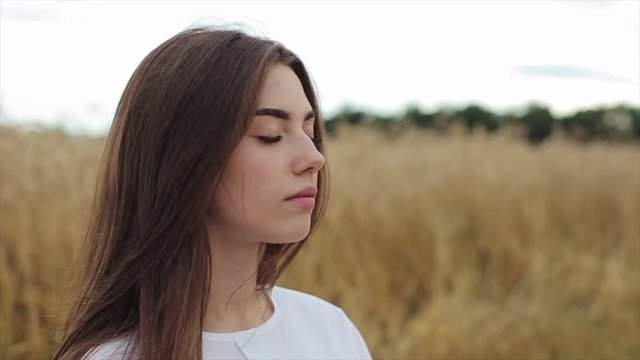 A beautiful young girl with long hair stands with closed eyes on a wheat field. Meditation in nature. Close-up. Slow motion
