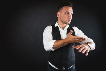 A handsome, young man, dressed in a white shirt and a cardigan from a suit on a dark background, is in a hurry or late, indicating the time, impatience, upset and angry for the delay. Time concept