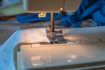A close up of the needle of a sewing machine stitching material together to make a homemade face mask as people are required to wear them due to Covid 19
