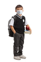 Schoolboy in a uniform holding books and an apple and wearing a protective face mask