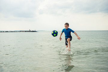 Happy handsome teen boy running and playing with ball in neoprene swimsuit in sea