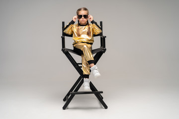 a little girl in gold suit sits on a chair. Isolated on a yellow background