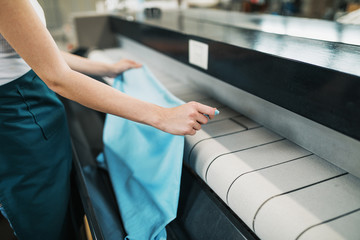 Young laundry worker pats the linen on the automatic machine at the dry cleaners.