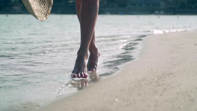 Close-up of legs of a woman walking on water along the beach.