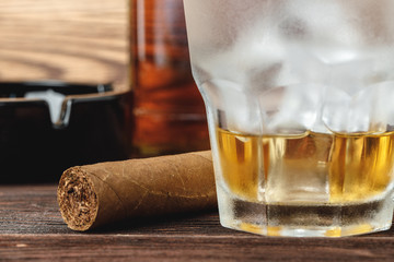 Glass of whiskey and rolled cigars on wooden table
