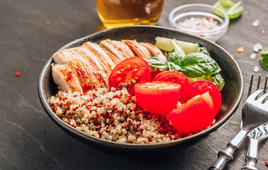 Healthy salad bowl with quinoa, tomatoes, chicken, cucumber and basil on black wooden background. Superfoods.