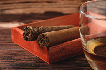 Red wooden box with rolled cigars on wooden table close up