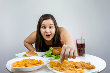 woman sits at a table and eats dinner in which fast food: French fries, burger, chicken leg, chips