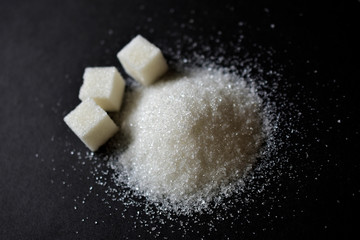 Scattered sugar in a pile and refined sugar cubes on a black background