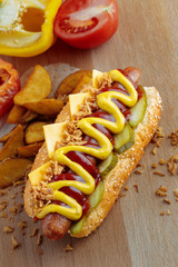 Hot dog with yellow mustard and ketchup on wooden board