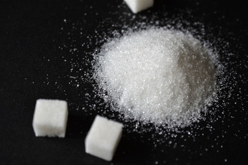 Obraz na płótnie Canvas Scattered sugar in a pile and refined sugar cubes on a black background