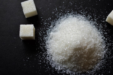 Scattered sugar in a pile and refined sugar cubes on a black background