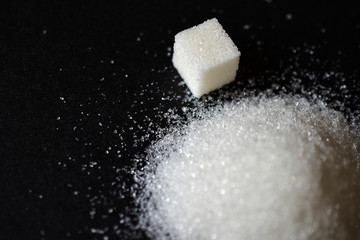 Scattered sugar in a pile and refined sugar cubes on a black background