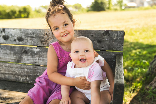 Happy adorable chubby baby girl sitting on a bench with her daughter sister