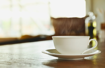 A white cup of coffee with white smoke on wooden top table