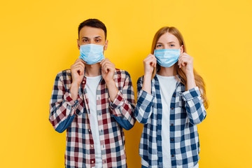 man and woman dressed in checked shirts and medical masks to protect against viruses, standing on an isolated yellow background, Quarantine, coronavirus, protection