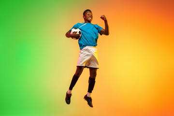 High jumping winner. Male soccer, football player training in action isolated on gradient studio background in neon light. Concept of motion, action, ahievements, healthy lifestyle. Youth culture.