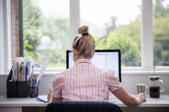 Rear View Of Woman Working From Home On Computer  In Home Office