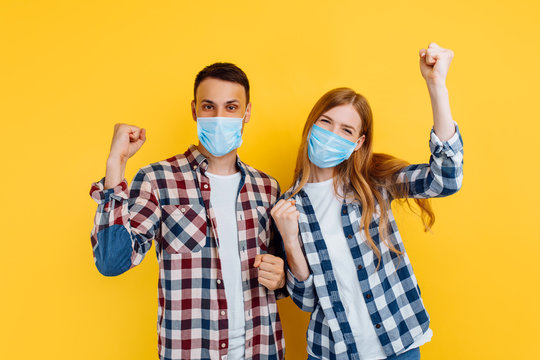 Happy Man And Woman With Medical Protective Masks On Their Faces, Have Fun And Show A Victory Gesture, Standing On An Isolated Yellow Background, Quarantine, Coronavirus, Protection