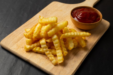 Tasty french fries with ketchup on cutting board, on the black table background