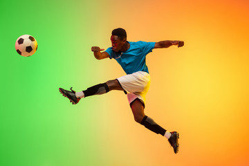 Fototapeta na wymiar High jumping. Male soccer, football player training in action isolated on gradient studio background in neon light. Concept of motion, action, ahievements, healthy lifestyle. Youth culture.